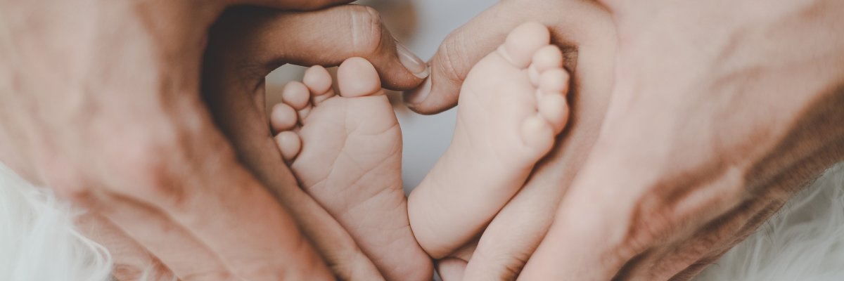 Zwei Personen umfassen die Füße eines Babys