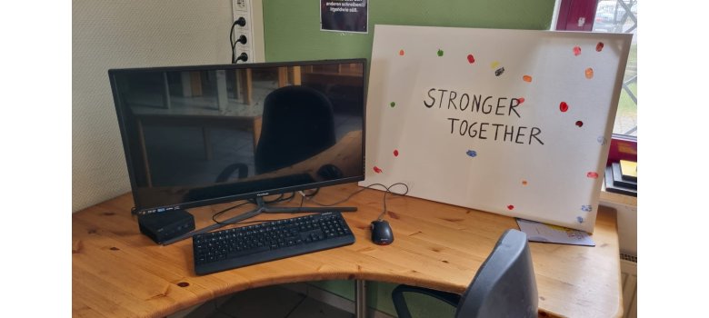 PC - daneben eine Leinwand mit den Worten "Stronger together"