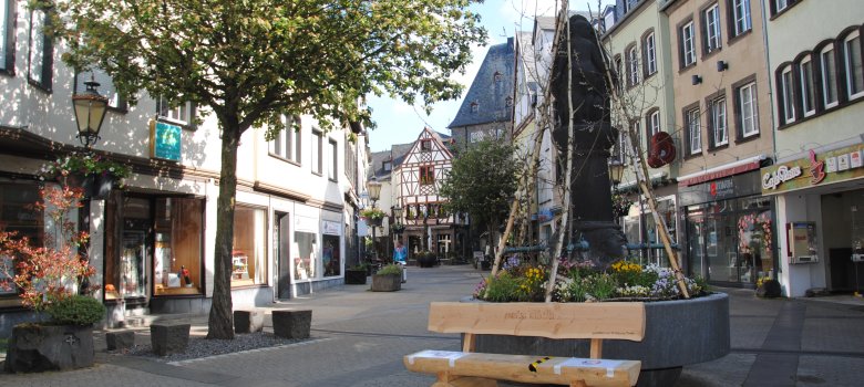 Blick in die Mayener Fußgönzerszone im Bereich Brückenviertel mit Holzbank, kleinen Geschäften und dem Brückentor