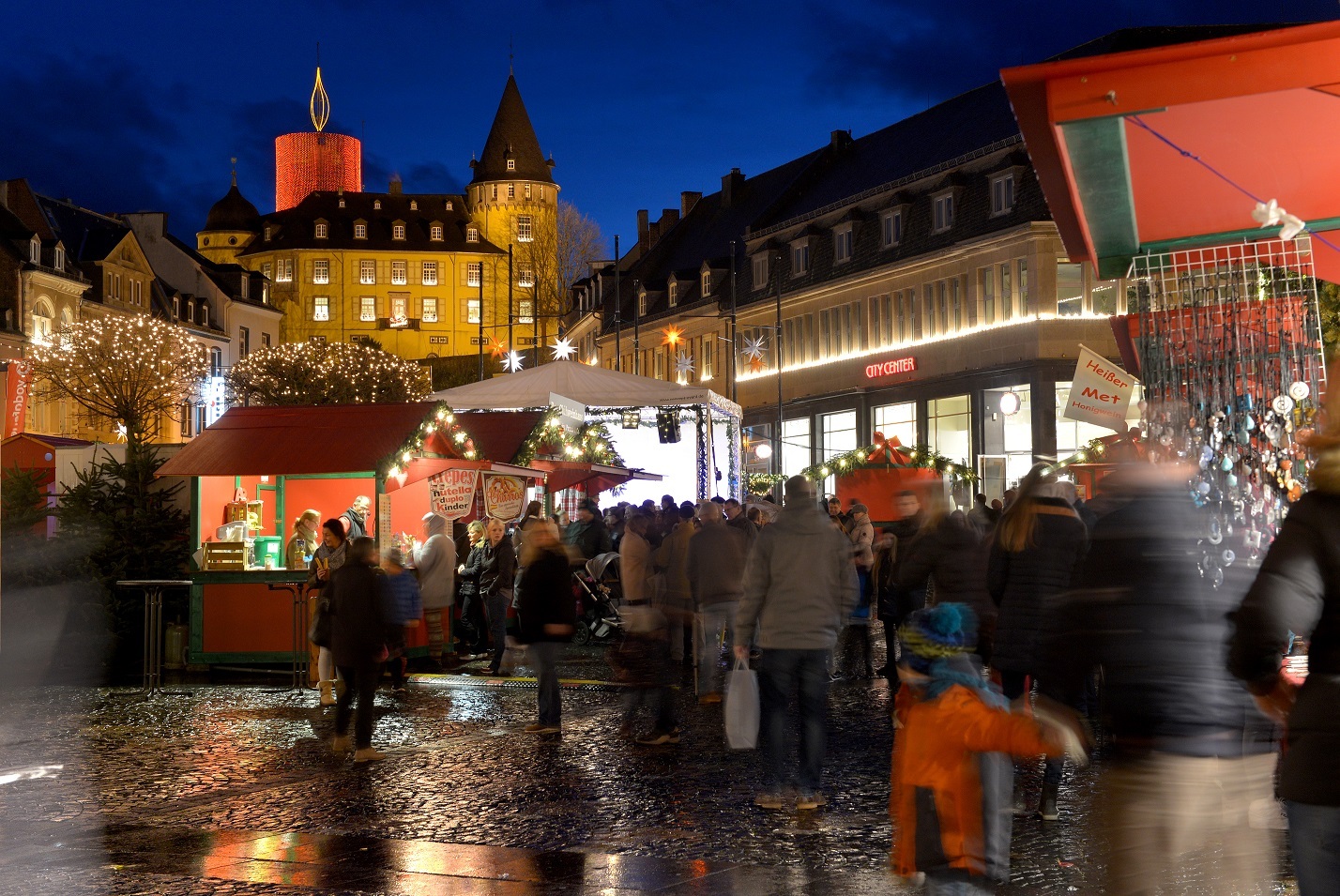 Nikolaus-Krammarkt_2 Marktstände am Abend mit einer Ansammlung von Menschen und der Genovevaburg im Hintergrund