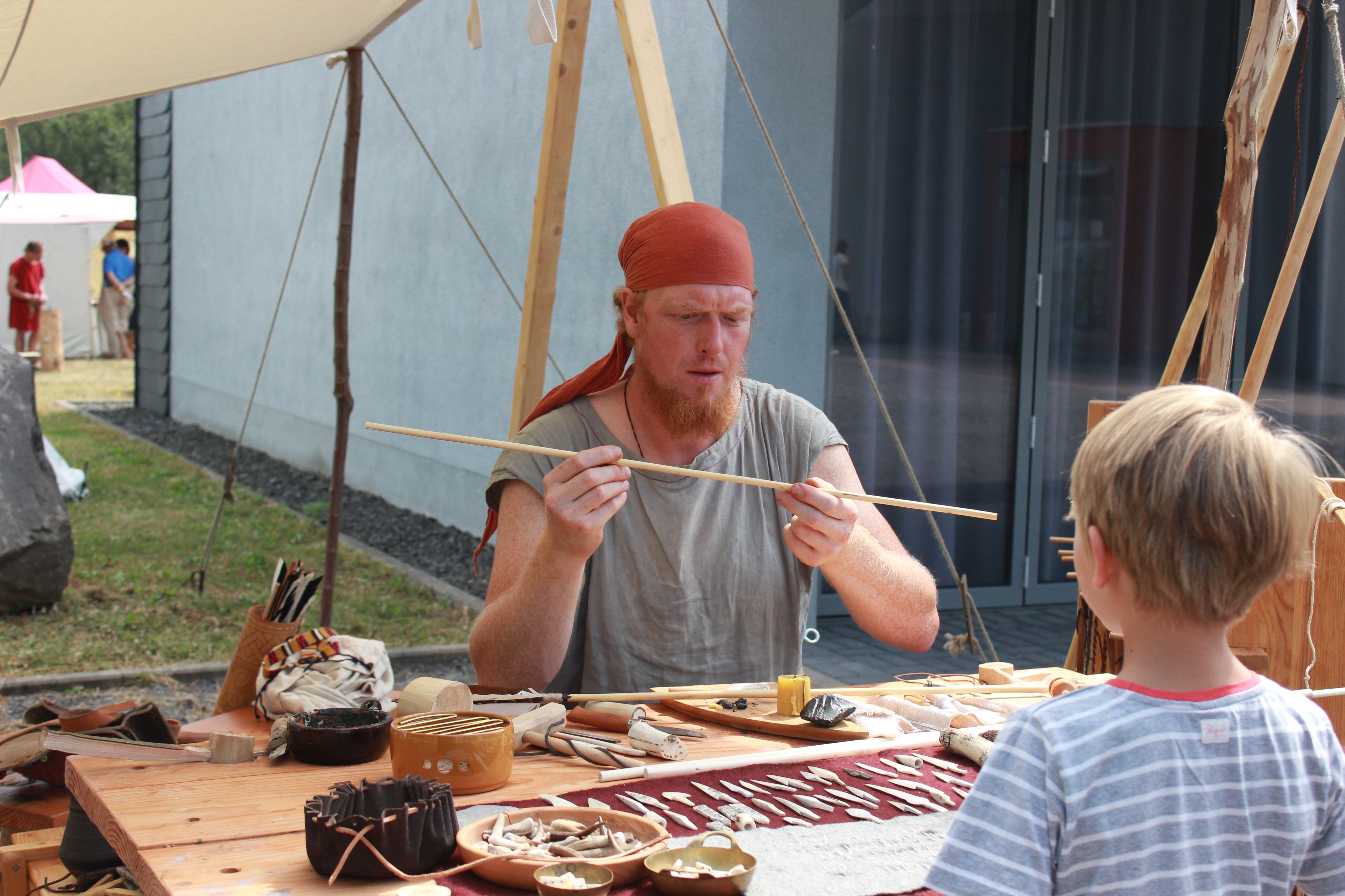 Kind schaut gespannt dem Pfeilemacher bei seiner Arbeit zu