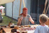 Kind schaut gespannt dem Pfeilemacher bei seiner Arbeit zu 