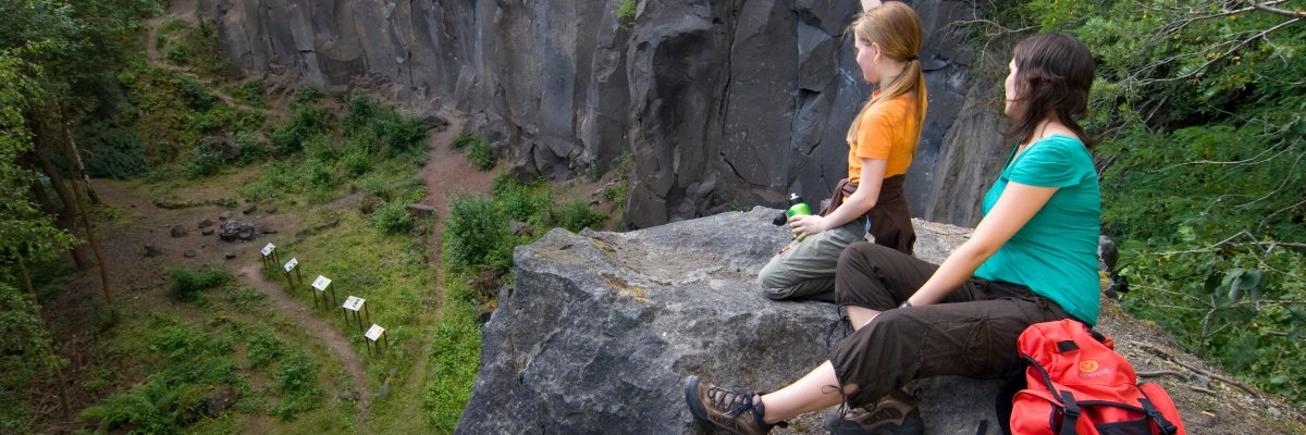 2 Wanderer sitzen auf einer Steinkuppe und blicken über den ehemaligen Steinbruch