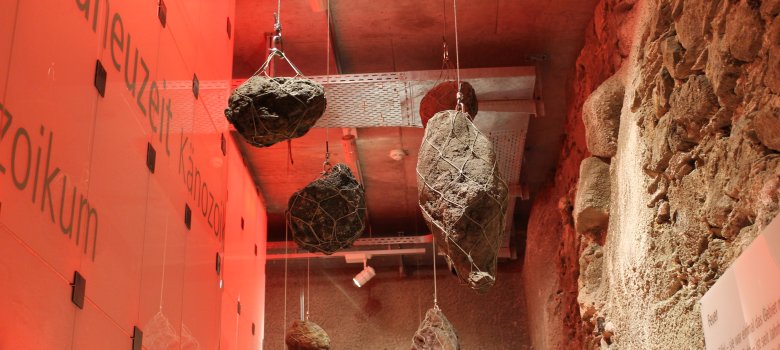 in rotes Licht getauchter Ausstellungsbereich Geologie mit von der Decke hängenden Steinen