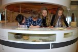 Kinder stehen hinter Theke und schauen sich Museumsstücke an