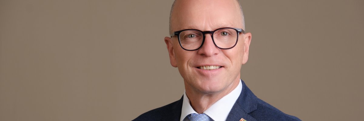 Oberbürgermeister Dirk Meid in einem dunkelblauem Anzug vor beigen Hintergrund
