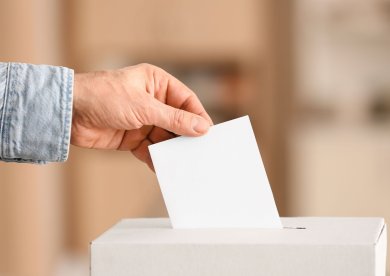 Hand mit Brief und Briefwahl Urne