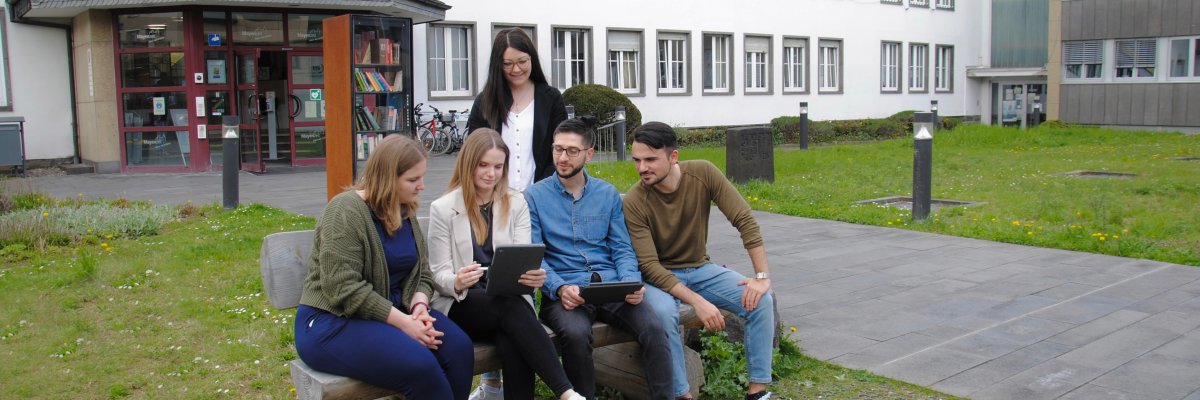 Eine Gruppe Junger Menschen sitzen auf Bank vor dem Rathaus