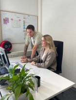 Stadtsekretär Frau sitzt an Schreibtisch, Mann steht daneben