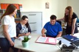 Vier Personen in einem Büro am Schreibtisch, die in einer Mappe lesen