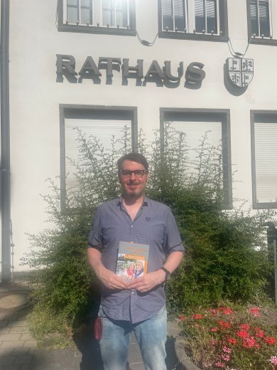 Tobias Härtling mit einer Broschüre in der Hand vor dem Rathaus