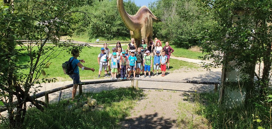 Kinder stehen vor Dinosaurier in der Landschaft