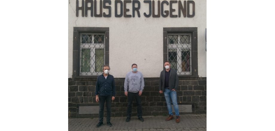 3 Männer mit Maske und genügend Abstand stehen vor einem weißen Haus mit der Aufschrift Haus der Jugend.