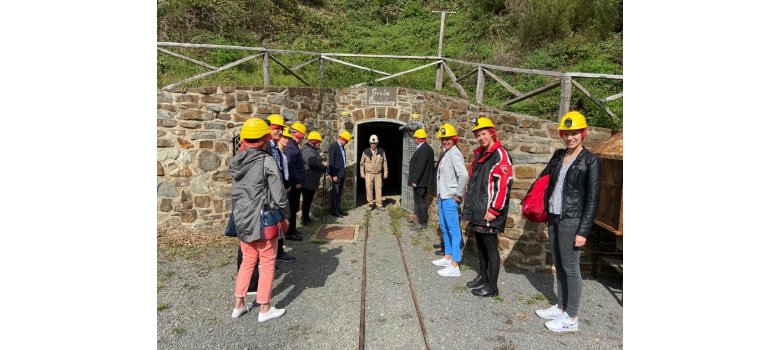 Mehrere Personen mit Gelben Helmen stehen vor dem Eingang einer Grube  