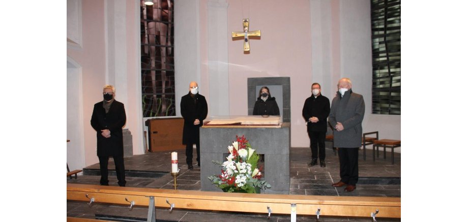 5 dunkel gekleidete Personen mit Abstand aufgestellt in einer Kirche