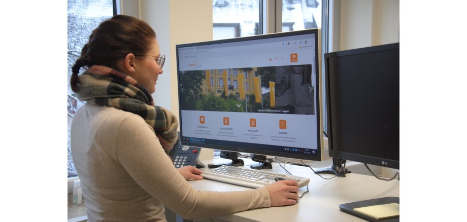Eine Person steht am Bürotisch vor einem großen Monitor und die neue Website ist auf dem Bildschirm zu sehen.