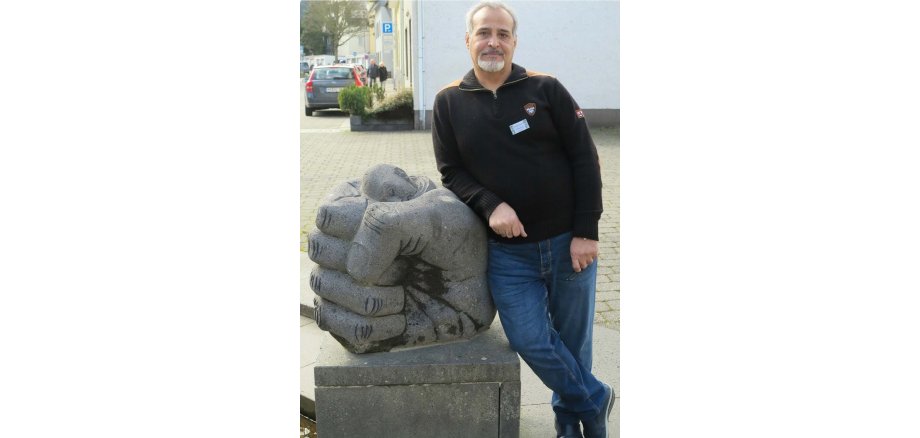 Mo.T. steht an seiner Skulptur aus Basalt, die eine Faust mit einem traurig blickenden Mann zeigt, ist auf dem Platz vor dem Alten Arresthaus
