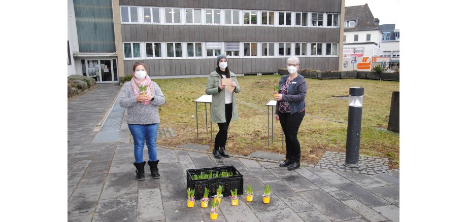 Drei Frauen stehen vor der Stadtverwaltung und halten Osterglocken in der Hand zum Weltfrauentag 