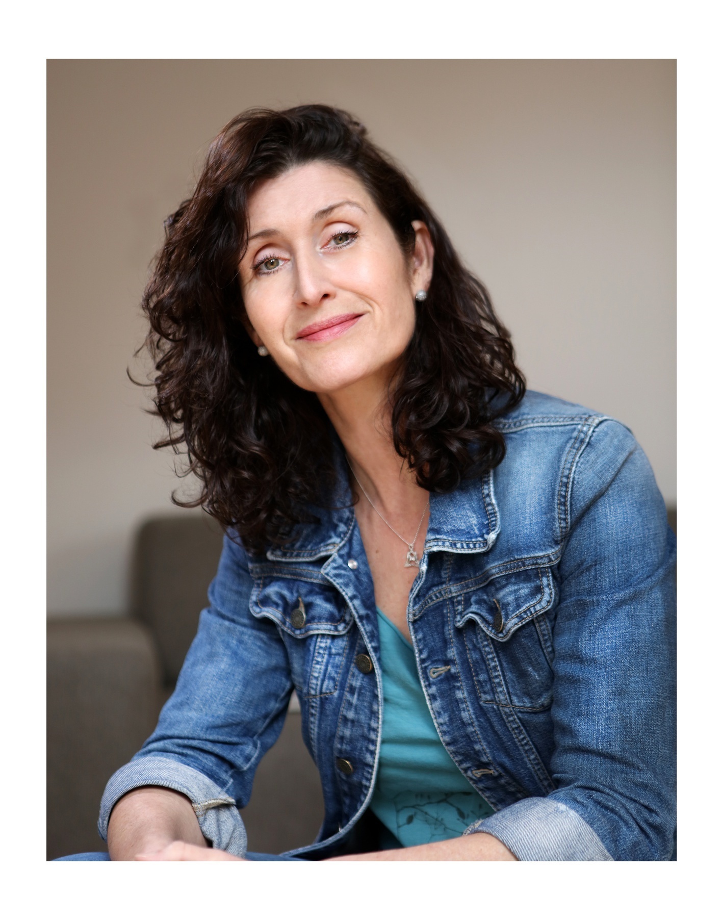 Frau Sabine Brandauer hat dunkles mittel langes Haar und trägt ein blaues Shirt mit einer Jeansjacke darüber