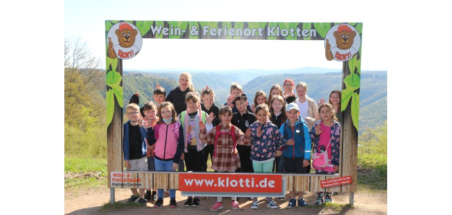 Auf dem Bild ist eine Gruppe Kinder mit Betreuern hinter einem Fotopanorama vom Ferienort Klotten zu sehen