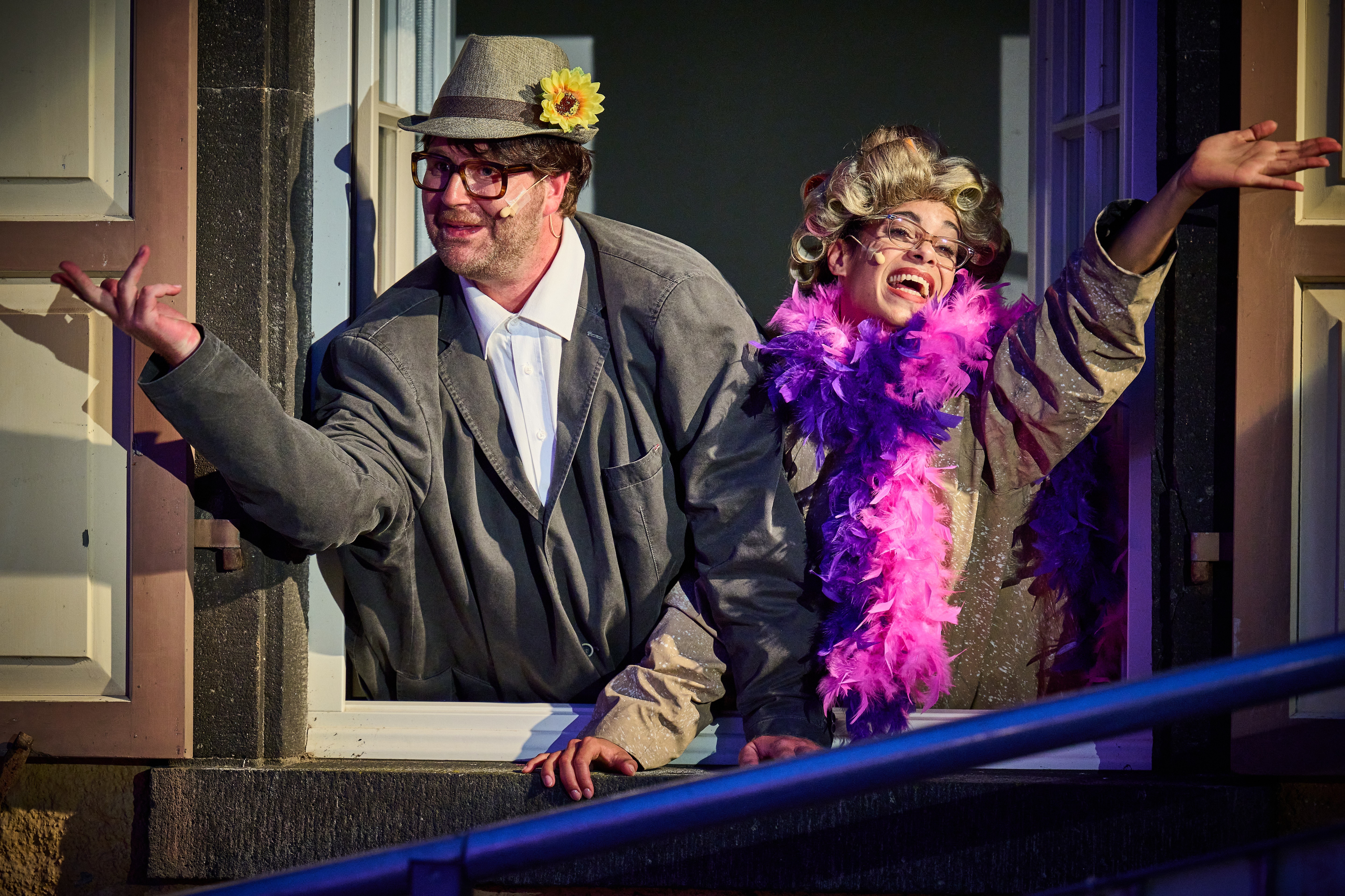 Zwei Personen stehen an einem offenen Fenster und schauen raus. Jeweils ein Arm ist rausgestreckt