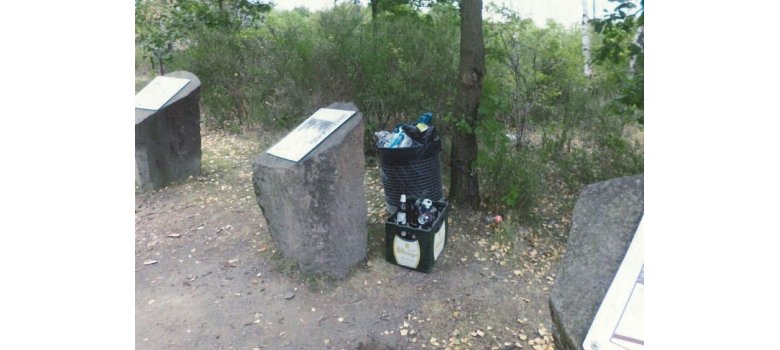 Vor einem überfüllten Mülleimer steht eine Kiste mit leeren Bierflaschen