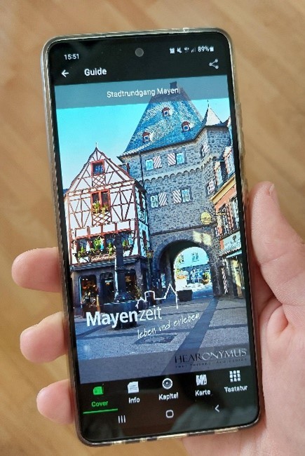 Handy in einer Hand mit Bildern von Mayen drauf 