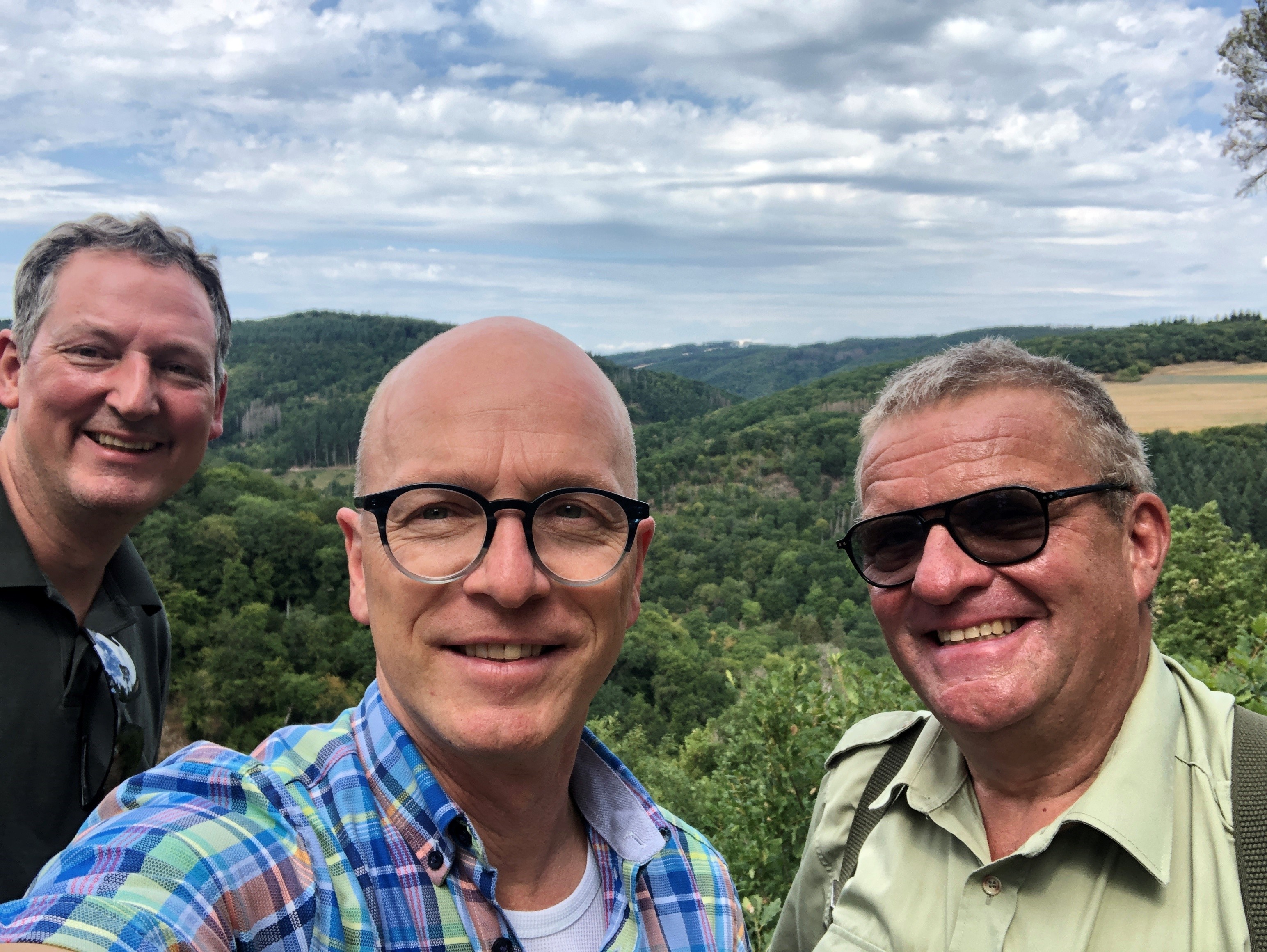 3 Personen machen ein Selfie vor einem Panorama des Mayener Stadtwaldes. Der Himmel ist bewölkt
