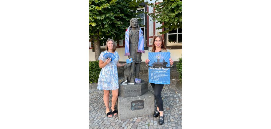 Zwei Personen stehen mit allen Merchandise Produkten am Mayener Jung auf dem Marktplatz