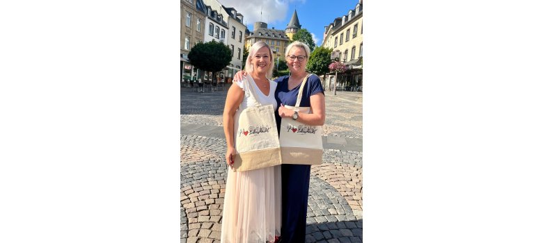 Zwei Personen stehen auf dem Marktplatz vor der Genovevaburg. Die zwei Frauen haben die Lukasmarkt Stofftasche umhängen und stehen im Arm