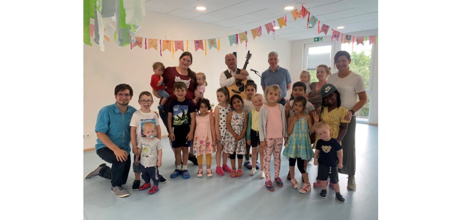 Betreuer und eine Gruppe Kinder stehen fröhlich zusammen und lächeln in die Kamera. Ein Mann hält eine Gitarre in den Händen