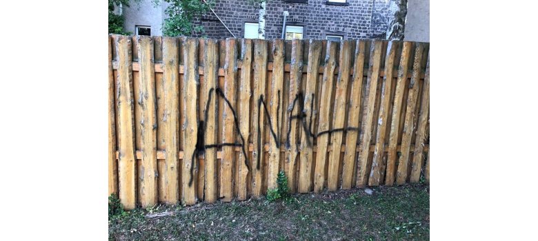 Ein Zaun mit schwarzem Graffiti besprüht