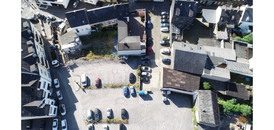 Eine Aufnahme von oben - man sieht einen Parkplatz mit Autos, Innenhöfe und Dächer von Häusern