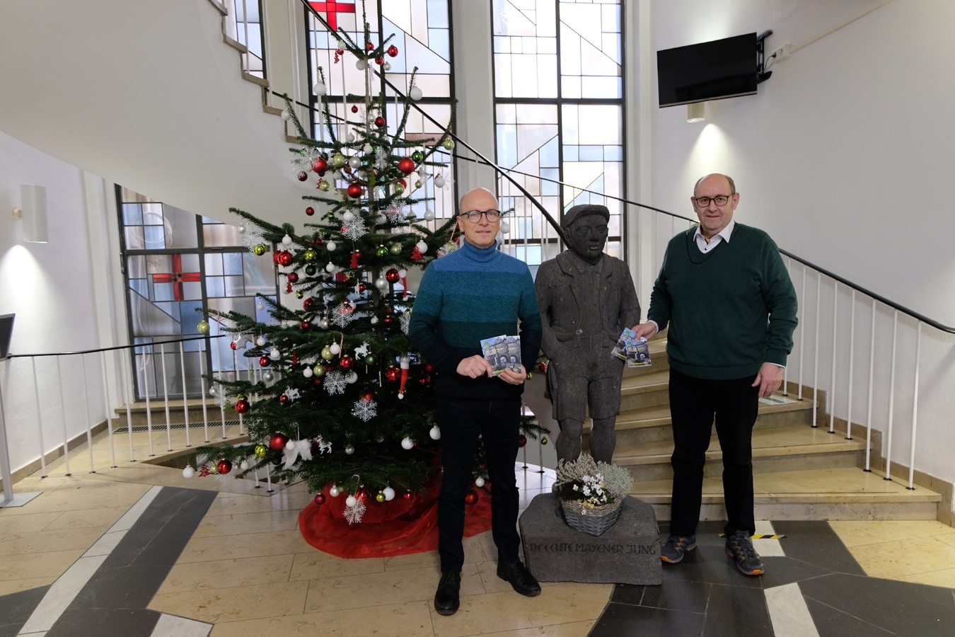 2 Personen mit Plänen in der Hand vor dem Weihnachtsbaum im Eingangsbereich des Rathauses