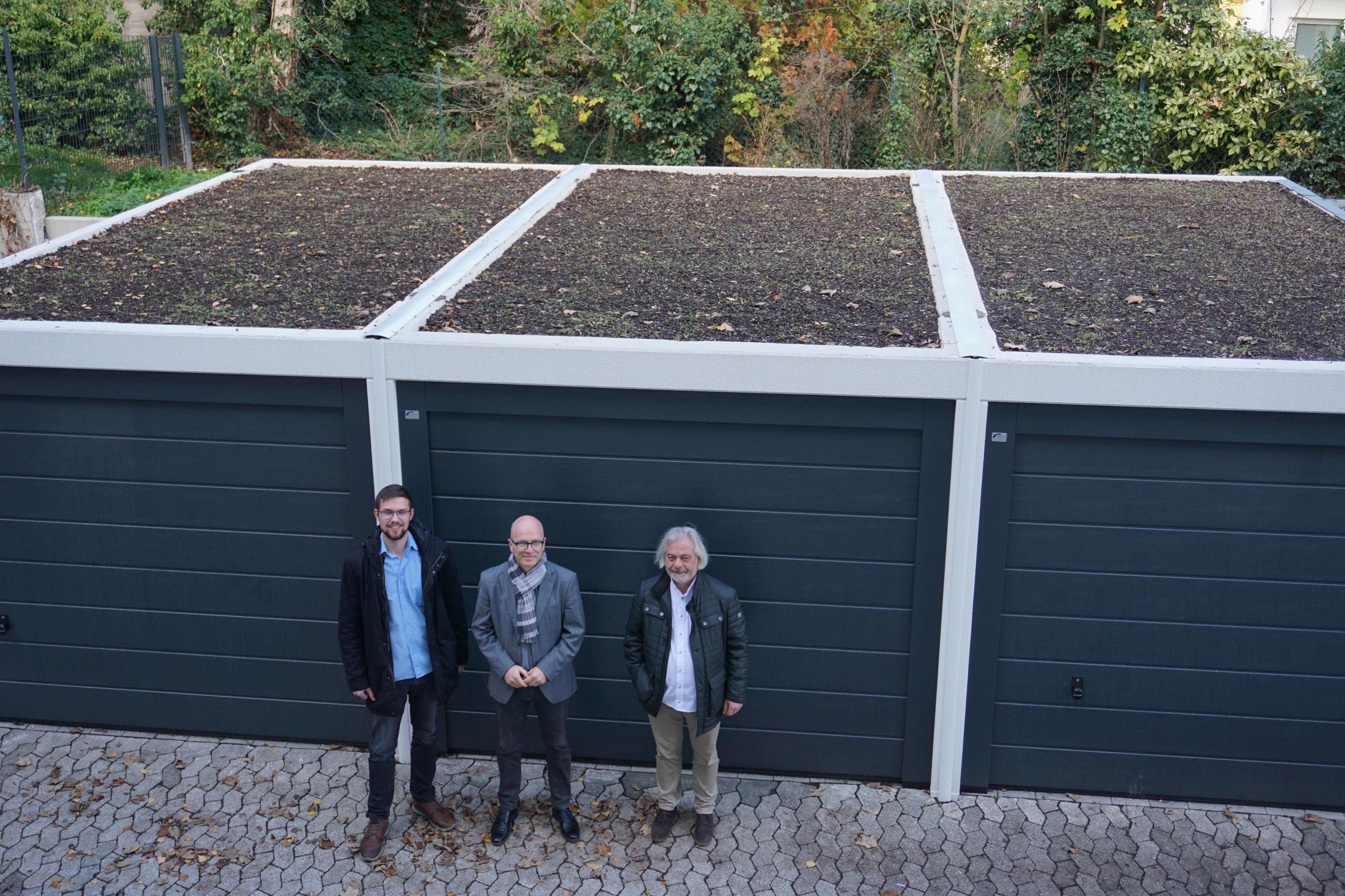 3 Personen stehen vor 3 Garagen. Man kann die Dachbegrünung gut erkennen