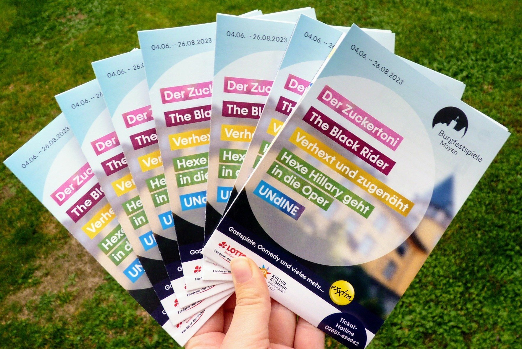 7 Flyer in einer Hand vor grünem Hintergrund