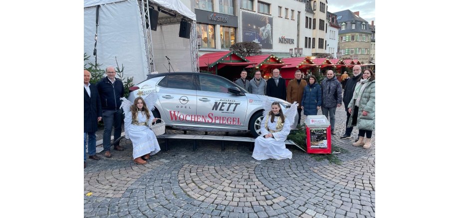 Ein silbernes Auto - darum stehen einige Menschen zu einem Gruppenbild zusammen