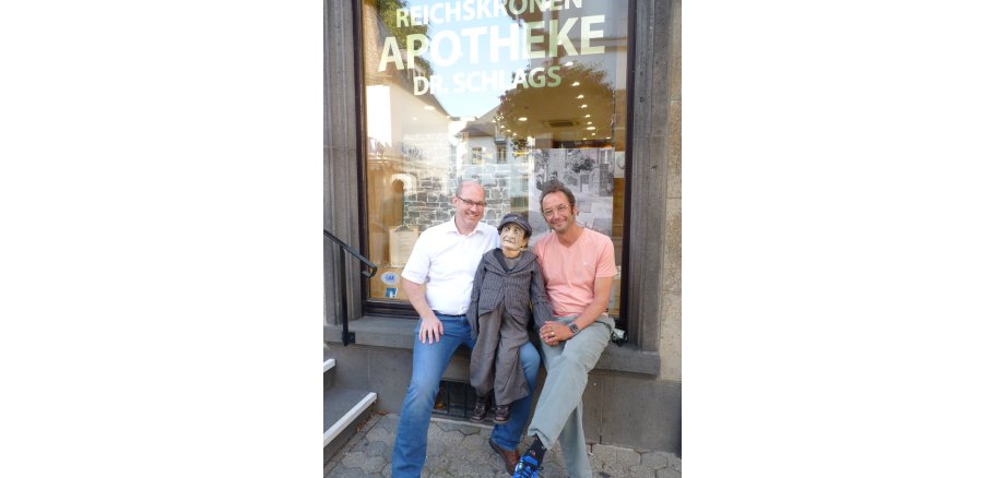 Wolfgang Schlags und Alexander May mit der Puppe auf der Fensterbank vor dem Schaufenster der Apotheke