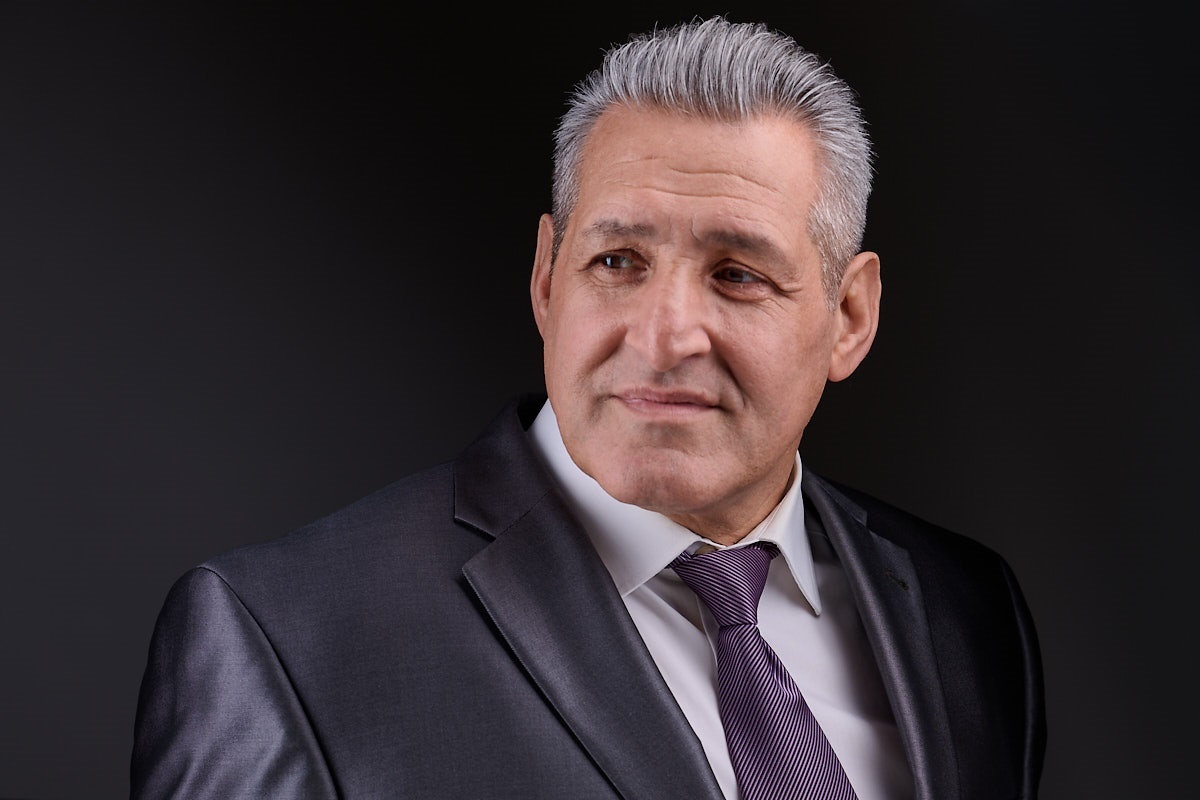 Ein Mann im Anzug, weißem Hemd und lila Krawatte vor schwarzem HIntergrund