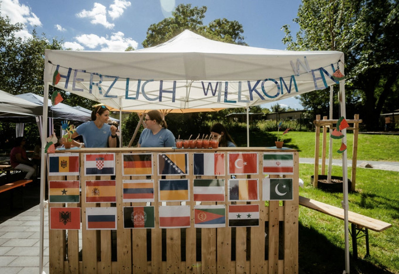 Ein Pavillon mit verschiedenen Flaggen und zwei Frauen hinter der Getränkeausgabe