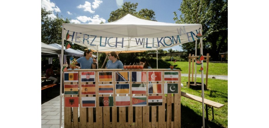 Ein Pavillon mit verschiedenen Flaggen und zwei Frauen hinter der Getränkeausgabe