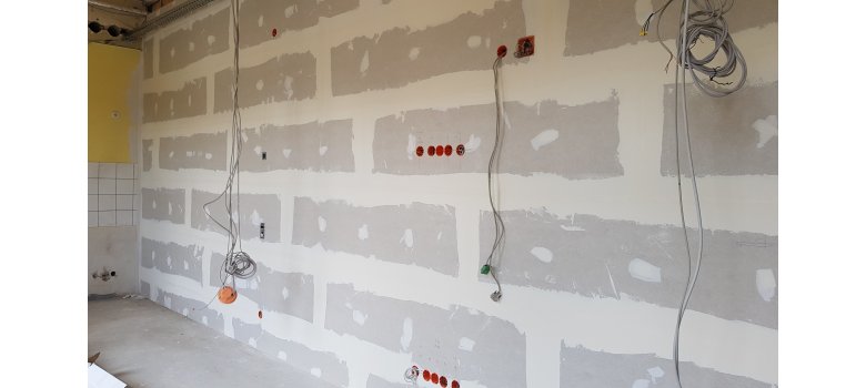 Eine Wand die noch unverputzt ist. Es hängen Kabel aus der Wand