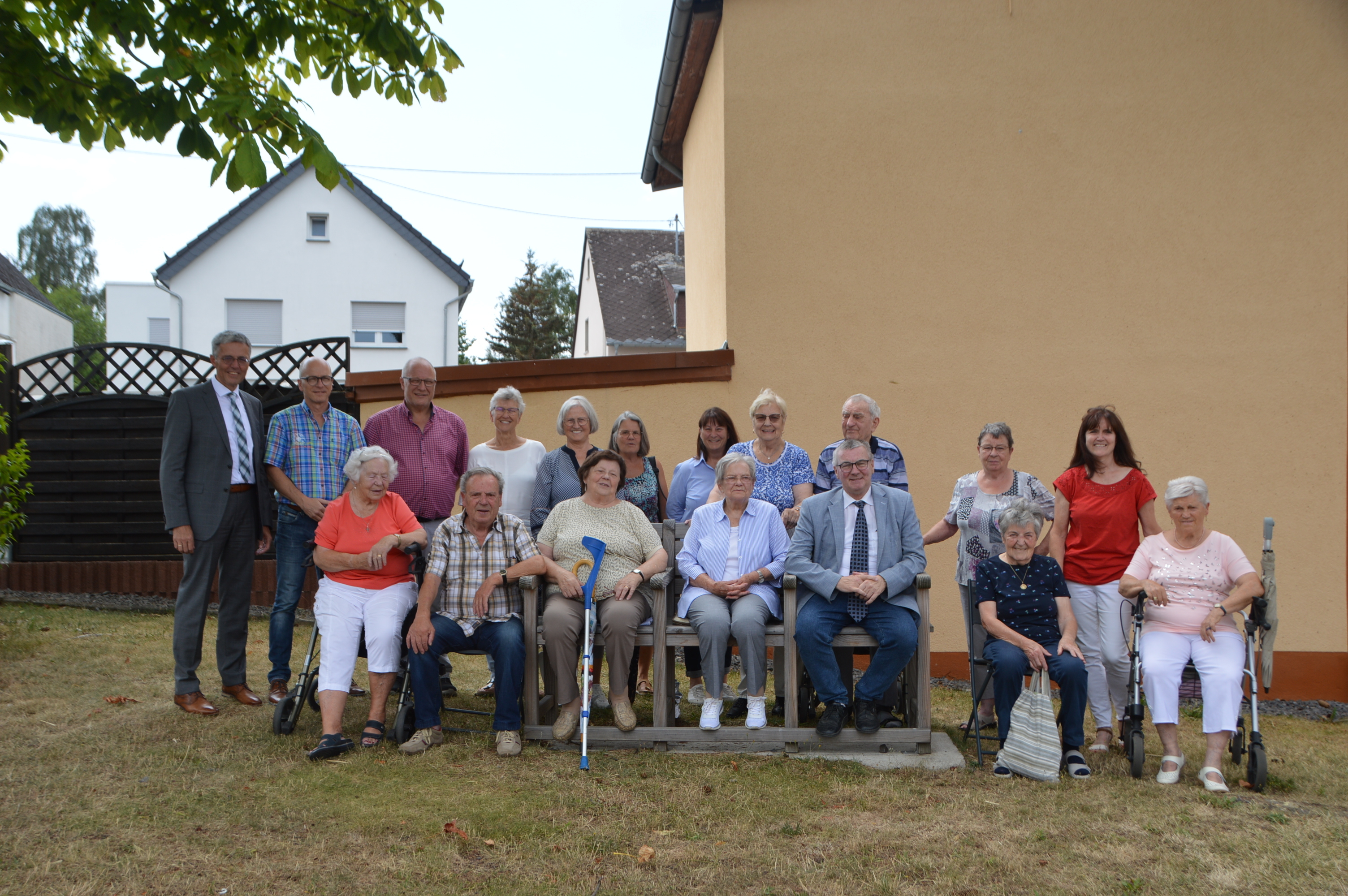 Zahlreiche Rentnerinnen und Rentner sitzen auf der neuen Bank und stehen hinter der Bank