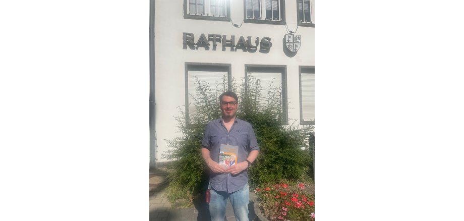 Tobias Härtling mit einer Broschüre in der Hand vor dem Rathaus