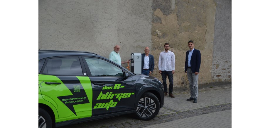 Ortsvorsteher Siegmar Stenner, Oberbürgermeister Dirk Meid, Klimaschutzbeauftragter der Stadt Mayen Helge Lippert und Fabian Vocktmann als Regionalvertreter der Westenergie an einer Ladeseule vor dem neuen E-Dorfauto.  