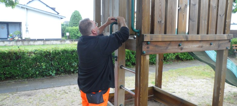 Zwei Personen reparieren eine Rutschbahn auf dem Spielplatz