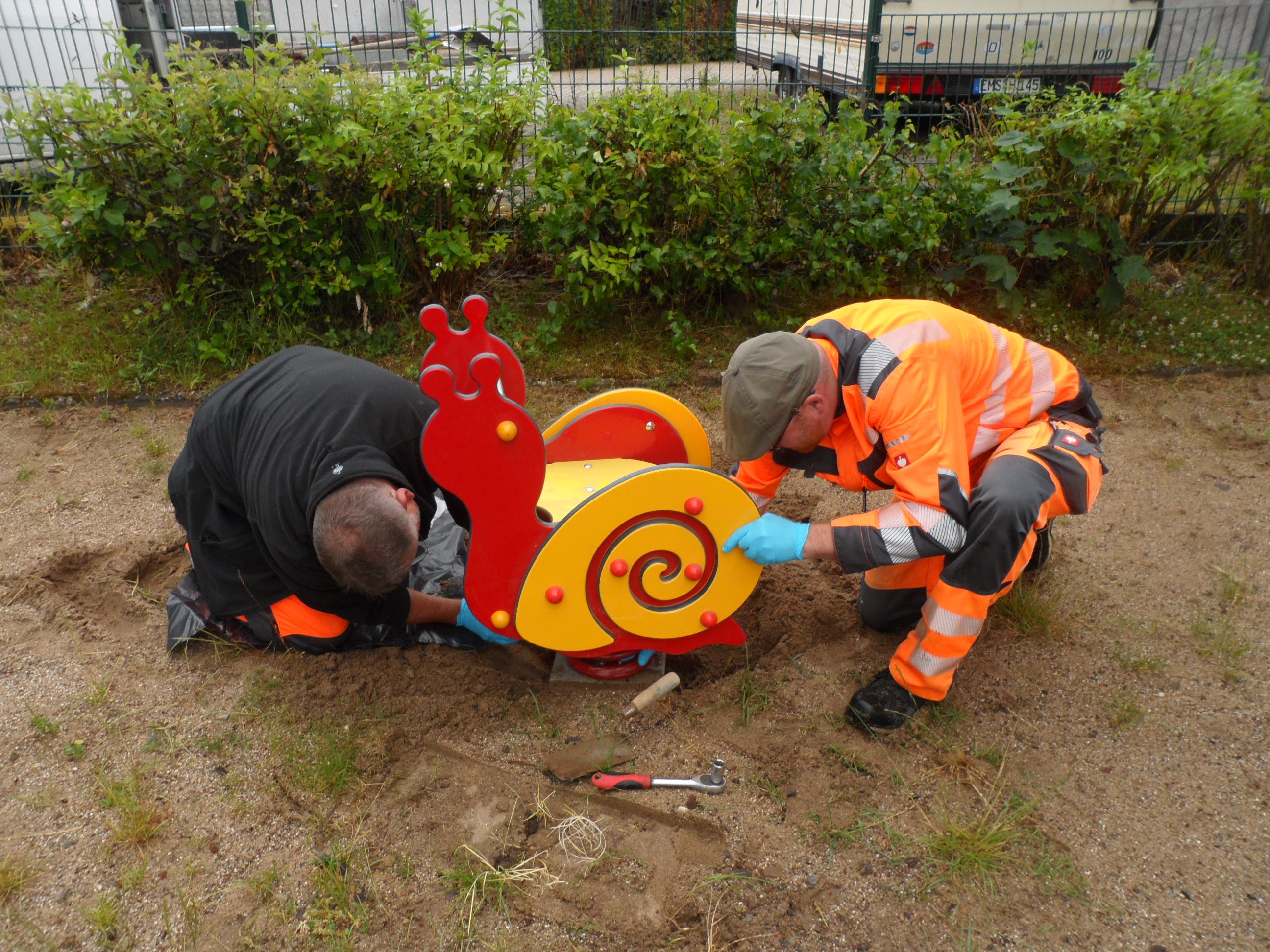 Zwei Personen reparieren ein Spielgerät auf einem Spielplatz