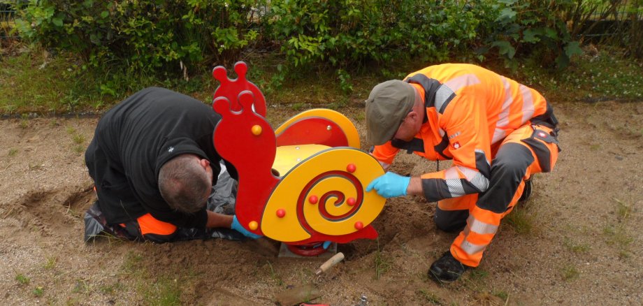 Zwei Personen reparieren ein Spielgerät auf einem Spielplatz