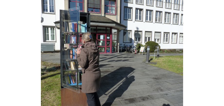 Jetzt im Mayener Bücherschrank nach interessanten Büchern stöbern! Frau steht vor Bücherschrank vor der Stadtverwaltung Mayen