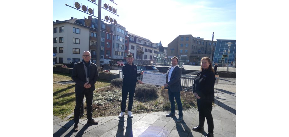 4 Personen stehen vor dem Rathaus für einen Spendencheck im Hintergrund ist die Rosengasse zu sehen.